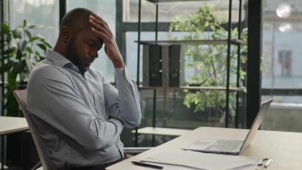 過労アフリカ系アメリカ人の成熟した男性オフィスでノートパソコンを作業疲れ目の緊張に苦しんで疲れ男性高齢者のビジネスマン痛み不快感頭痛片頭痛健康問題を感じる — ストック動画