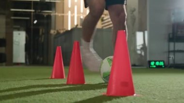 Tanınmayan futbolcu spor salonunda külahlar arasında top sürüyor profesyonel sporcu futbolcu adam futbol sahasında idman yapıyor erkek kaslı bacakları yakın mesafeden gol atıyor.