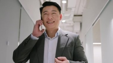 Orta yaşlı Asyalı iş adamı ofis koridorunda cep telefonuyla konuşan akıllı telefonlu, gülümseyen Koreli, Japon bir adamın cep telefonunu araması.