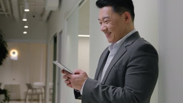 亚洲成熟的商人笑着浏览手机在线商务社交网络发短信用智能手机应用互联网聊天中年男子在公司办公室笑 — 图库视频影像