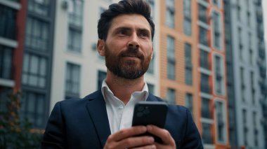 Beyaz, yakışıklı, profesyonel iş adamı orta yaşlı bir adam şehir dışında cep telefonu işi yapıyor cep telefonuyla sohbet ediyor SMS okuyor e-bankacılık uygulaması ekommerce modern teknoloji kavramını kullanıyor
