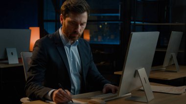 Orta yaşlı profesyonel iş adamı Kafkasyalı işçi erkek yetişkin patron öğretmen evrak işlerinde çalışıyor evrak işleri bilgisayardaki ödeme faturalarıyla arama verileri yazıyor notlar yazıyor.