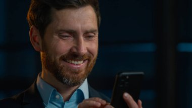 Caucasian bearded man businessman professional middle-aged employer hold cellphone mobile gadget chatting distant communication on phone read sms use smartphone bank app pay online e-commerce service