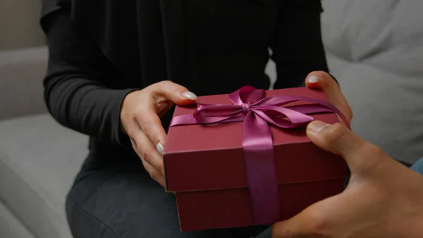 Close up presenting gift on marriage anniversary Valentine love day romantic date unrecognizable female hands unpacking surprise pink box take off ribbon. Cropped view couple man and woman get present