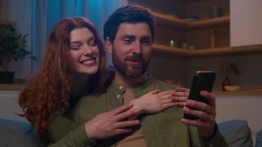 Kafkasyalı mutlu bir çift video konuşması yapıyor. Evde telefon kullanıyor. Mutfakta el sallıyor, aşık bir kadını selamlıyor.