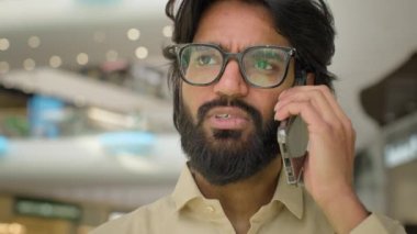 Ciddi Hispanik Hintli iş adamı gözlüklü Arap sakallı adam cep telefonuyla konuşan akıllı telefon konuşmaları cep telefonuyla konuş ve kapalı alanda görüşme emri ver.