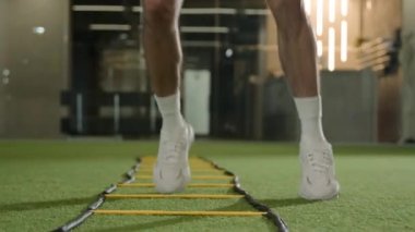 Profesyonel futbolcu merdivenler arasında zıplıyor spor salonunda koşuyor tanınmayan sporcu futbolcu antrenman koordinasyonu erkek kaslı bacaklarının yakın plan futbol sahasında topa vuruyor.