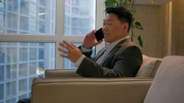 Asyalı mutlu iş adamı cep telefonunu arayan Çinli bir Japon modern şirkette oturmuş gülümseyen orta yaşlı bir girişimci telefon görüşmelerine cevap veriyor.