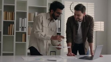 İki çok ırklı iş ortağı gülümseyen adam dizüstü bilgisayarla iş projesini tartışıyor. El sıkışma ortaklığı anlaşmasının finansal faydalarını gösteriyor. Ofis toplantısı, el sıkışma, başarı takım çalışması.