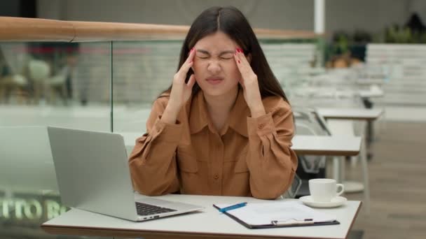 疲れたアジア人の女性がノートパソコンの書類作成の問題でカフェで働くビジネスの難しさ病気不健康な中国人の韓国人のビジネス女性は痛みを伴う頭の頭痛片頭痛が痛い緊張過労を被る — ストック動画