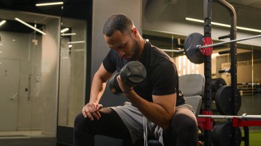 Spor salonunda biceps egzersizi yapan Afrikalı Amerikalı bir adam spor kulübünde güçlü vücut geliştirme sporu yapan güçlü bir sporcu ağır halter ağırlığı kaldıran ağırlık kaldırma antrenmanı yapan bir vücut geliştirme uzmanı.