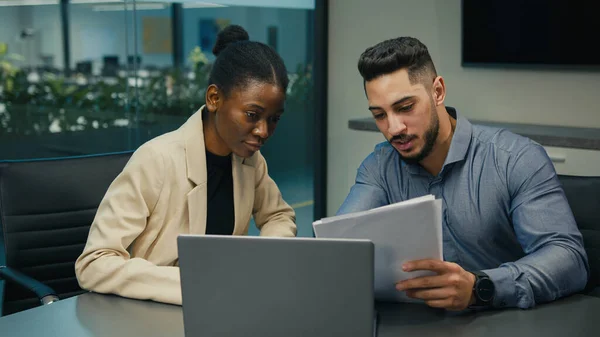 Diverse business colleagues Indian Arabian man and African American woman working discuss financial data analyzing documents corporate paper project result in report with laptop talk at office meeting