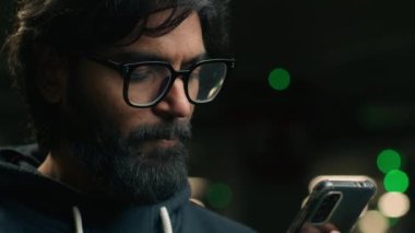 Yeraltı otoparkında gece karanlığında gözlüklü Hintli sakallı bir adam cep telefonu uygulaması kullanıyor sosyal medyada sohbet ediyor Müslüman bir erkek akıllı telefon taksisi kullanıyor.