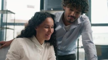 Hintli Arap erkek lider akıl hocası, İspanyol kadın stajyere online dizüstü bilgisayarda yardım öğretiyor. İş grafikleri, çok ırklı takım çalışması, iş kadını iş kadını gülümsemesi, ofiste yapılan konuşmaları açıklıyor.