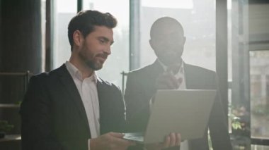 Neşeli çok ırklı iş arkadaşları Kafkasyalı yönetici ve Afrikalı Amerikalı yatırımcı iki mutlu iş adamı dizüstü bilgisayarlarıyla şirketlerin beyin fırtınası projesini tartışıyorlar.