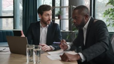 Ofis toplantısında laptoplu iki farklı iş adamı ve çok ırklı ortaklar. Kafkas erkek iş adamı Afrikalı Amerikalı müşteri yatırımcısına yazılım danışmanlığını açıkladı