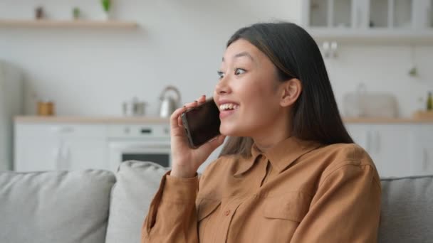 兴奋的亚洲女商人在厨房里讲电话听着好消息吃惊的是 一个讲手机的中国女孩喜欢打电话讨论新闻笑笑得胜 — 图库视频影像