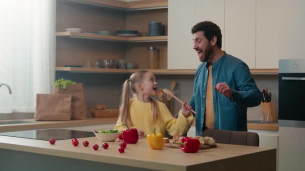 快乐的家庭在厨房里玩乐白种人爸爸在跳舞有趣的活跃的舞蹈小女孩在勺子里唱歌小女孩在厨房里唱歌小勺话筒在一起做饭 — 图库视频影像