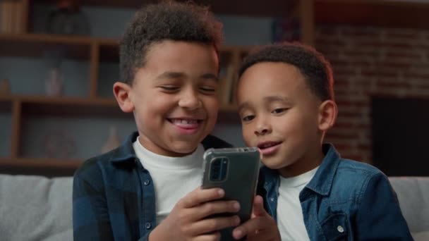 2アフリカ系アメリカ人の小さな男の子の兄弟は 現代の技術に中毒幸せな笑いの子供たちの兄弟は 唯一の親のコントロールなしで面白いスマートフォンアプリを使用して携帯電話ゲームをオンラインでプレイ — ストック動画