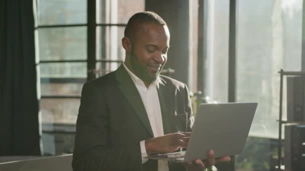 成熟的中年企业家商人非裔美国人在阳光灿烂的公司办公室与笔记本电脑搜索数字数据浏览网站快乐的男性高管看着相机微笑 — 图库视频影像