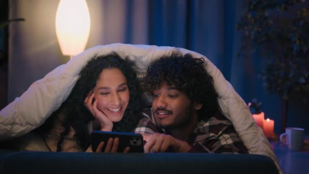 多种族男女情侣在家中使用手机震惊于网上新闻震惊纳闷智能手机社交媒体晚上躺在沙发上盖着毛毯小玩意成瘾 — 图库视频影像