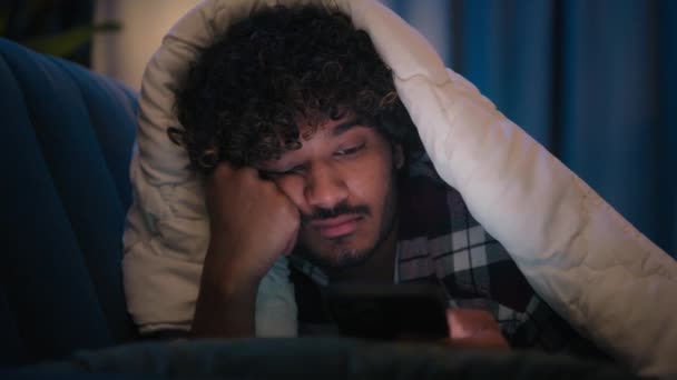 悲しいです眠い男Latino Tired Man Visedアラビア語睡眠昼寝退屈なインディアン男性に夜暗い家で毛布カバーの下にDuvetスクロール携帯電話中毒スマートフォン退屈ソーシャルメディア — ストック動画