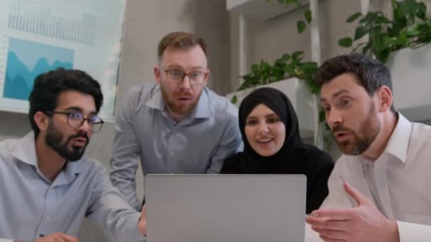 在办公室庆祝笔记本电脑成功的快乐的多种族同事在财务增长方面大获全胜 阿拉伯裔白人男子和穆斯林女子在Hijab队取得的成绩 — 图库视频影像