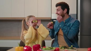 Mutfakta birlikte yemek yapan mutlu bir aile. Kafkasyalı kız çocuğu. Babasıyla oynaşıp salatalık dilimleri yapıyor.