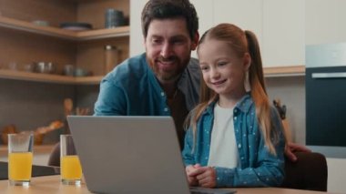 Bakıcı baba, küçük kızına çevrimiçi görevle yardım ediyor. Ev mutfağında dizüstü bilgisayarda yazılım eğitimi veriyor. Bilgisayarda e-öğrenim yapan mutlu çocuk ailesini açıklıyor.