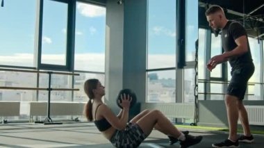 Spor kadını spor salonu zemininde yoğun egzersiz. Kadın sporcu kaslı kadın. Kafkasyalı erkek sporculara tıp topu atıyor.