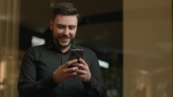 満足した白人男性実業家は 企業のオフィスで携帯電話を使用しますソーシャルメディアのテキストメッセージを読むスマートフォンアプリを閲覧チャットオンラインビジネスチャット男性男笑顔注文ウェブストアを作る — ストック動画