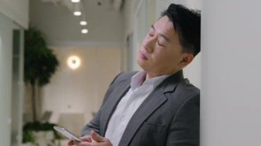 Yorgun Asyalı olgun adam yorgun 40 'lı yaşlarda Çinli işadamı cep telefonu sorunu yüzünden yorgun düşmüş ofis koridorunda yorgun erkek girişimci umutsuzluğa kapılmış cep telefonu uygulaması sorunu yaşıyor