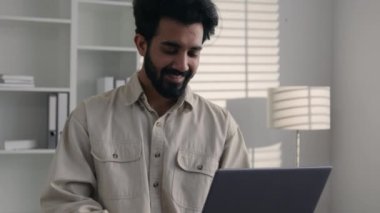 Müslüman Hintli işadamı ev ofisinden uzaktan çalışan gülümseyen Arap sakallı adam 30 'lu yaşlarda serbest çalışan bilgisayarlı iş adamı bilgisayarlı daktilo projesiyle internette mutlu erkek işçi gülümsemesi üzerine sohbet ediyor.