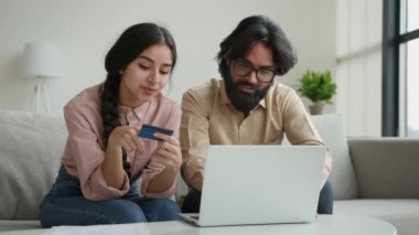 Arap Hintli Müslüman çift, oturma odasındaki koltukta oturuyor. Kredi kartı şifresi, bilgisayar bankacılığı uygulamasında geçiyor. Çevrimiçi çok ırklı kadın ve internet alışverişi yapıyor.