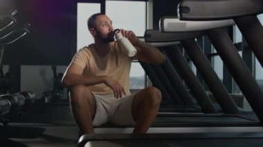 Spor şişesinden su içen yorgun adam spor salonunda koşu bandında koşu yaptıktan sonra tazelenen su dengesini yeniliyor. Afrikalı sporcu, Amerikan sporcusu vücut hidratı Latin atlet protein susuzluğu çekiyor.