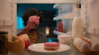 Bakış açısına göre, buzdolabının içinde aç Hintli bir erkek. Mutfak açık buzdolabında yemek isteyen Arap bir erkek. Isırılmış tatlı donut, gülümseyen bir gülümseme.