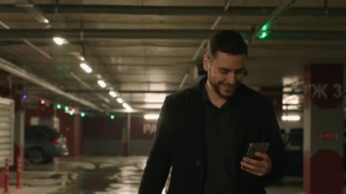 Memnun müşteri müşterisi Kafkasyalı şoför araba sahibi yer altında yürürken cep telefonu ekranına bak. Cep telefonu uygulaması kullan. Mesajda yetişkin gülümseyen işadamı akıllı telefonuyla dışarı çık.