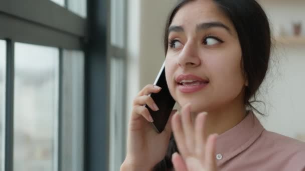 忧心忡忡的印度女商人会讲手机交谈商谈电话恼怒的女人谈论办公室窗口附近的智能手机通话解决了业务冲突的问题 — 图库视频影像
