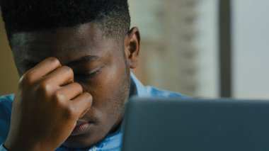 Tired exhausted businessman african american sick ill man 30s worker manager feel unwell headache eyestrain after computer work in office fatigue health problem lost online business project bad news