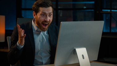 Mutlu Kafkasyalı adam orta yaşlı kıdemli iş adamı borsacı yönetici bilgisayarla çalışıyor karanlık gece ofisinde çalışıyor iyi haberler sunuyor online bahis kazanma kazancı zafere seviniyor