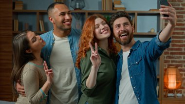 Adult caucasian bearded man blogger make group selfie photo with multiracial friends on mobile phone ethnic diversity people having fun at home smiling posing for smartphone camera union friendship
