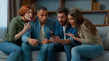 Surprised 30s middle-aged women men consumers read good news on mobile phone cellphone diverse ethnic friends multiracial people using virtual app smartphone indoors win business offer victory fortune