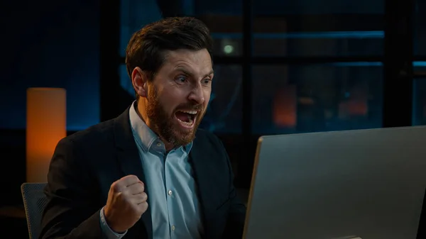 Annoyed angry businessman Caucasian middle-aged 40s man CEO employee mad furious crazy shouting fail online business project on computer trouble failure problem stress evening night office background