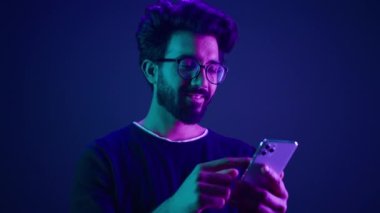 Arap erkek cep telefonuyla sohbet ediyor, akıllı telefonları tarıyor cep telefonuyla alışveriş siparişi veriyor Hintli adam Neon ultraviyole stüdyonun arka planında sosyal medya internet teknolojisi uygulaması kaydırıyor.