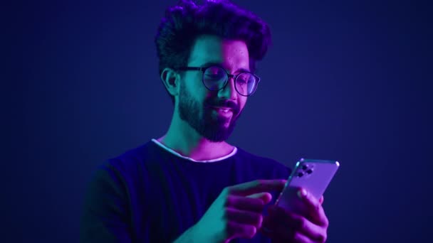 在霓虹灯紫外线工作室背景下 阿拉伯男性使用手机聊天浏览智能手机在线订购单游戏和手机印度男性滚动社交媒体网络应用 — 图库视频影像