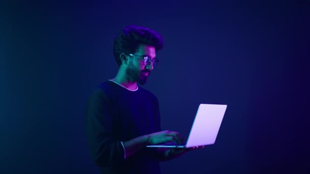 ネオン紫外線背景でラップトップを持つアラビア人男性インド人男性コーダープログラマー労働者ユーザーコンピュータコーディング現代的な技術親指を表示オンラインサービスの承認をお勧めします良いアプリ — ストック動画