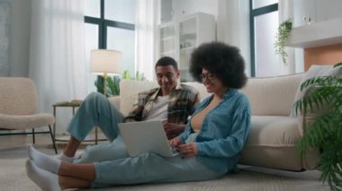 Afro-Amerikalı çift evlerinde dizüstü bilgisayarlarını kullanarak alışveriş yapıyor, faturaları ödüyor, ürünleri sipariş ediyor ve kendi evinde mutlu bir aile olarak beşlik jest yapıyor.