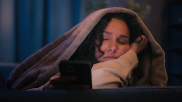 ヒスパニック疲労疲労疲れました昼寝眠い女の子ラティノ女性インド人女性アラビア人女性ブラウジング携帯電話チャットソーシャルメディア夜家で毛布カバーとともにDuvet睡眠昼寝睡眠 — ストック動画