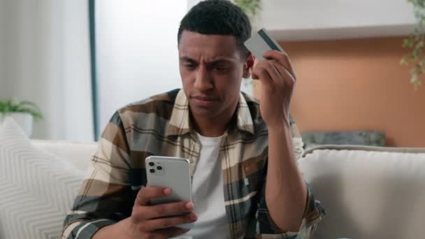 非洲裔美国人在沙发上对网上支付和信用卡银行破产感到很沮丧 他们想用手机和信用卡支付电子银行应用软件错误 — 图库视频影像