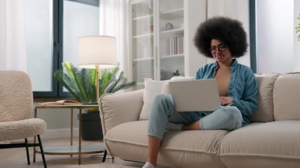 年轻的非洲裔美国女孩在离家很远的地方工作 带着笔记本电脑在沙发上工作 她是个自由撰稿人 用网络服务在沙发用户浏览网络上进行电子学习研究 在网上输入电子邮件 — 图库视频影像